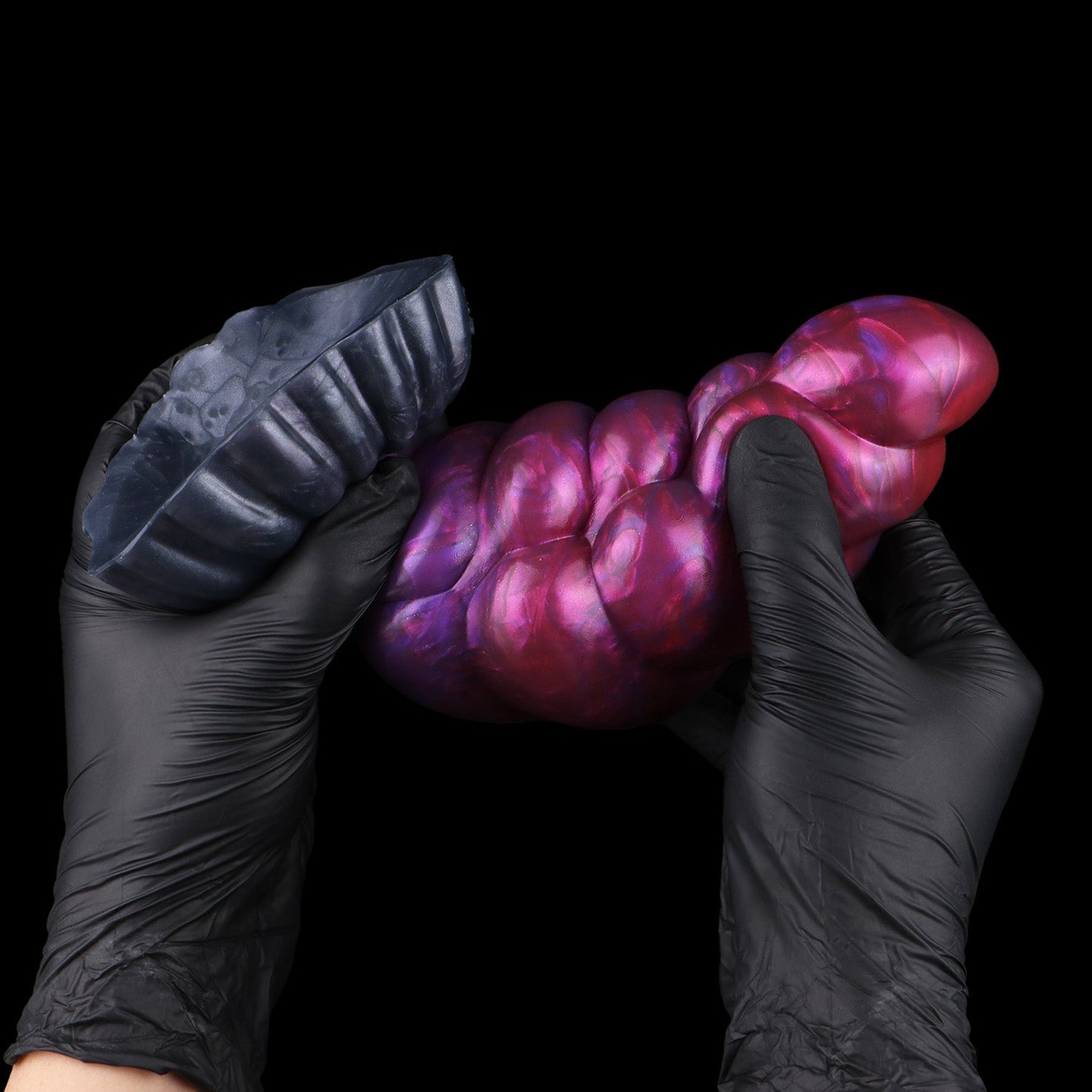 Larval the Alien Spawn dildo, Adrenaline colorway, flexed between two gloved hands to show the silicone's give