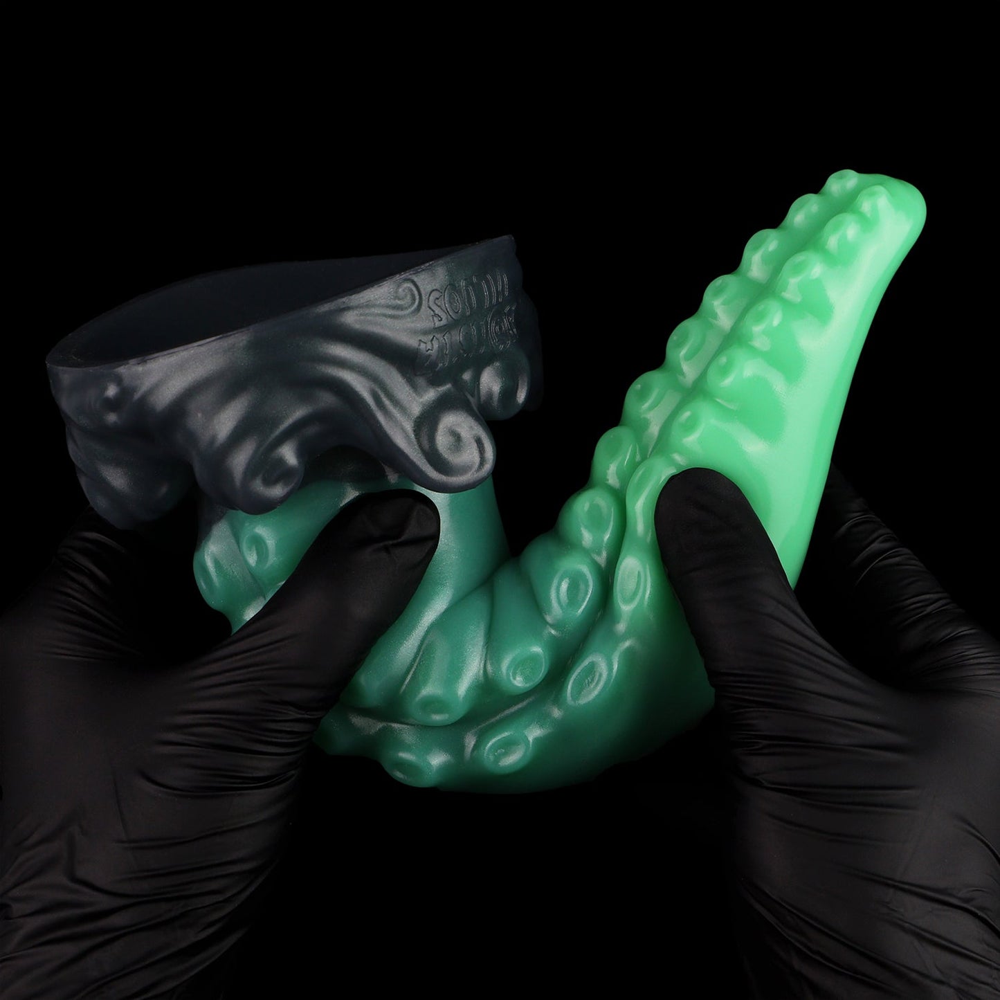Tendrul the Tentacle dildo, Ogre colorway, tentacle bent between two gloved hands to show the silicone's give